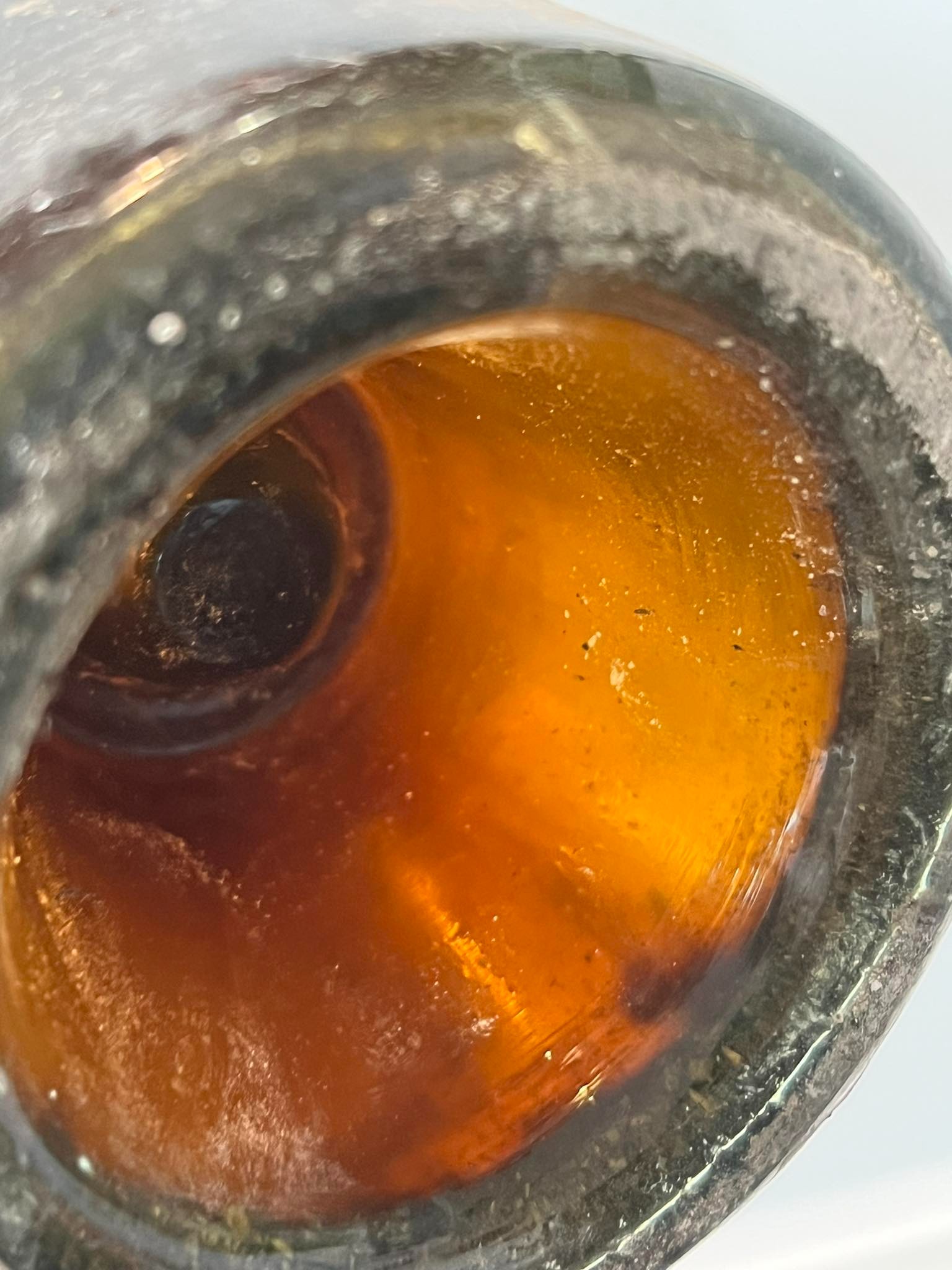 Base of the bottle seen through the glass, wine glowing amber in transmitted light