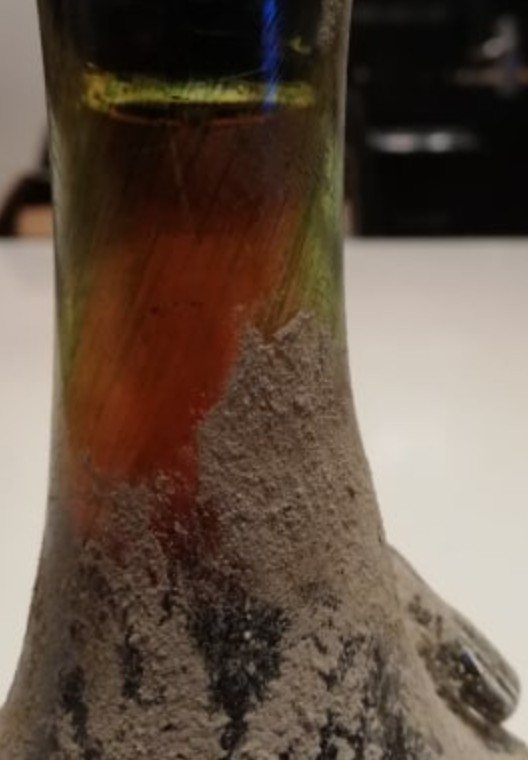Shoulder of a bottle showing green and red iridescence in the glass beneath cellar deposit