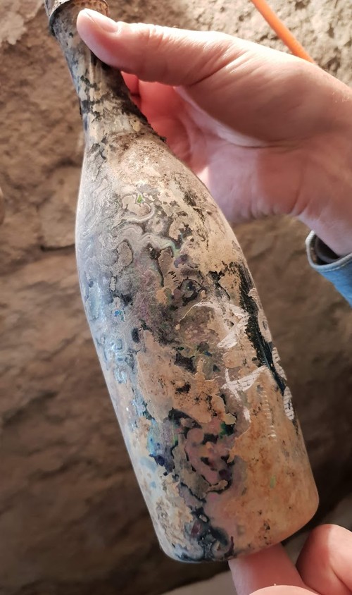 Bottle held in the hand, surface iridescent with cellar deposit