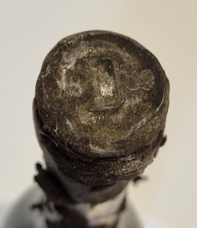 Lead capsule from above, a raised monogram within a plain circular border