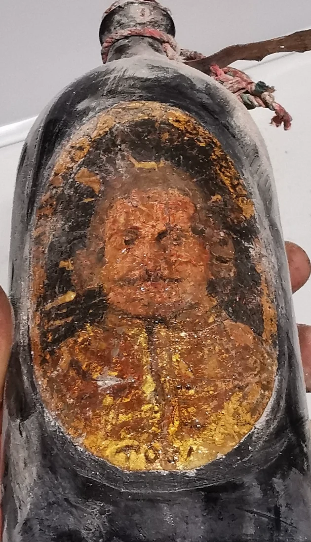 Painted portrait of a periwigged man on the body of a bottle, in an oval frame worked in gold and black