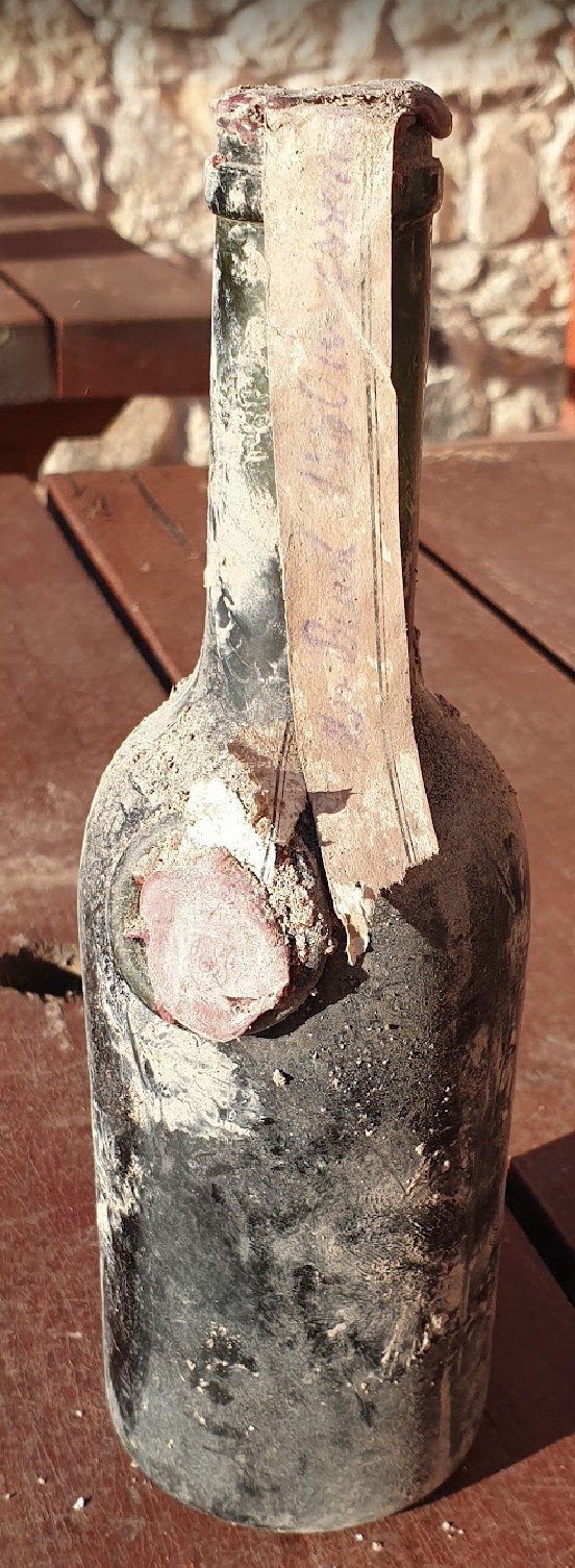 Handwritten paper strip running from the cork down the neck, fixed to the shoulder by a pink wax seal