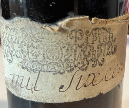 Torn label on a bottle, the stamp legended MOIEN PAPIER II SOLS LA FEUILLE and GEN. DE PARIS around crowned arms, handwriting reading “mil six cen…”