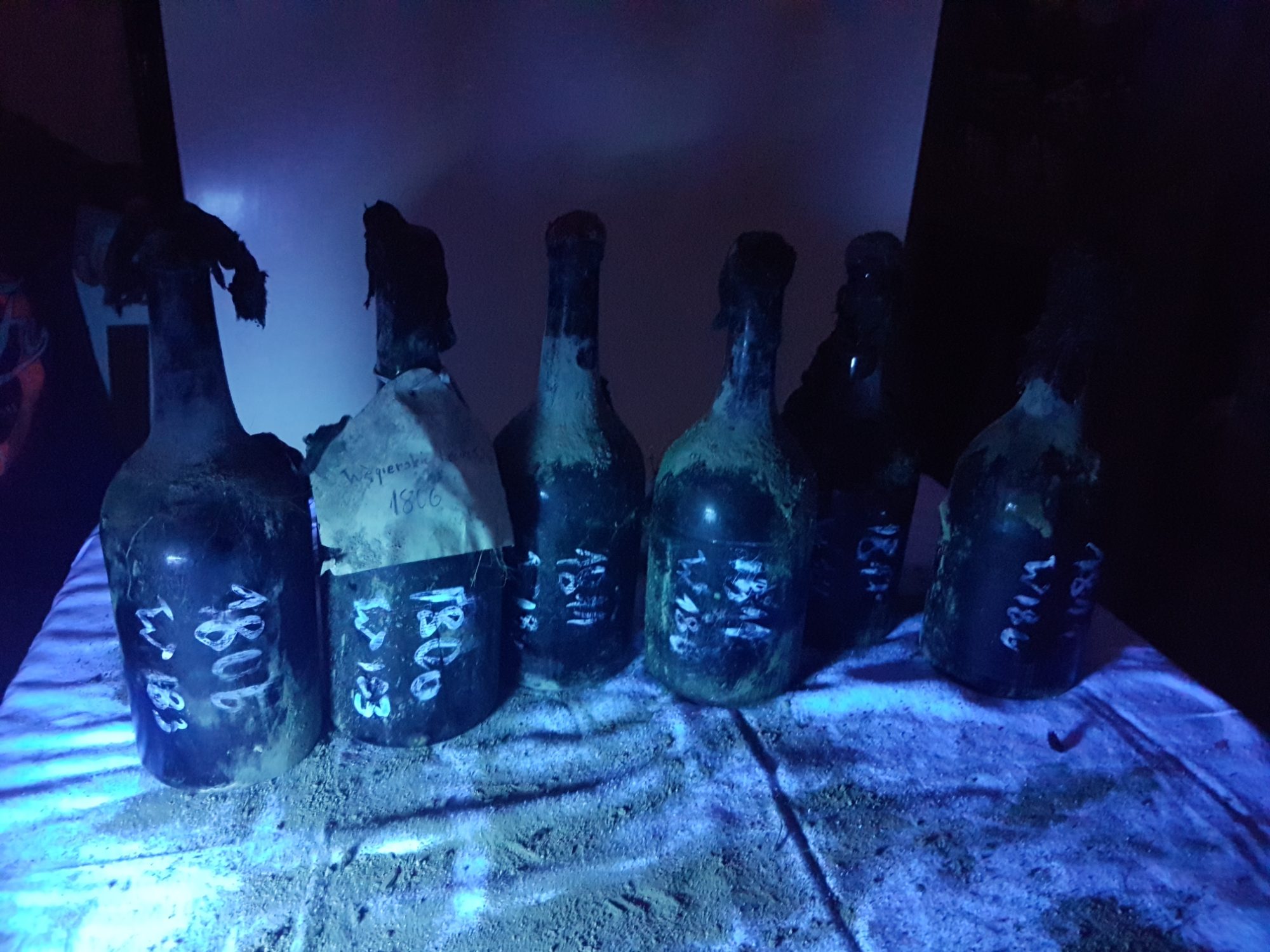 Six Fukier bottles under ultraviolet light, painted vintage numbers glowing