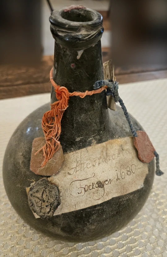 The 1680 onion bottle, near-black glass, parchment label and three wax seals on the shoulder, orange and blue cords at the neck