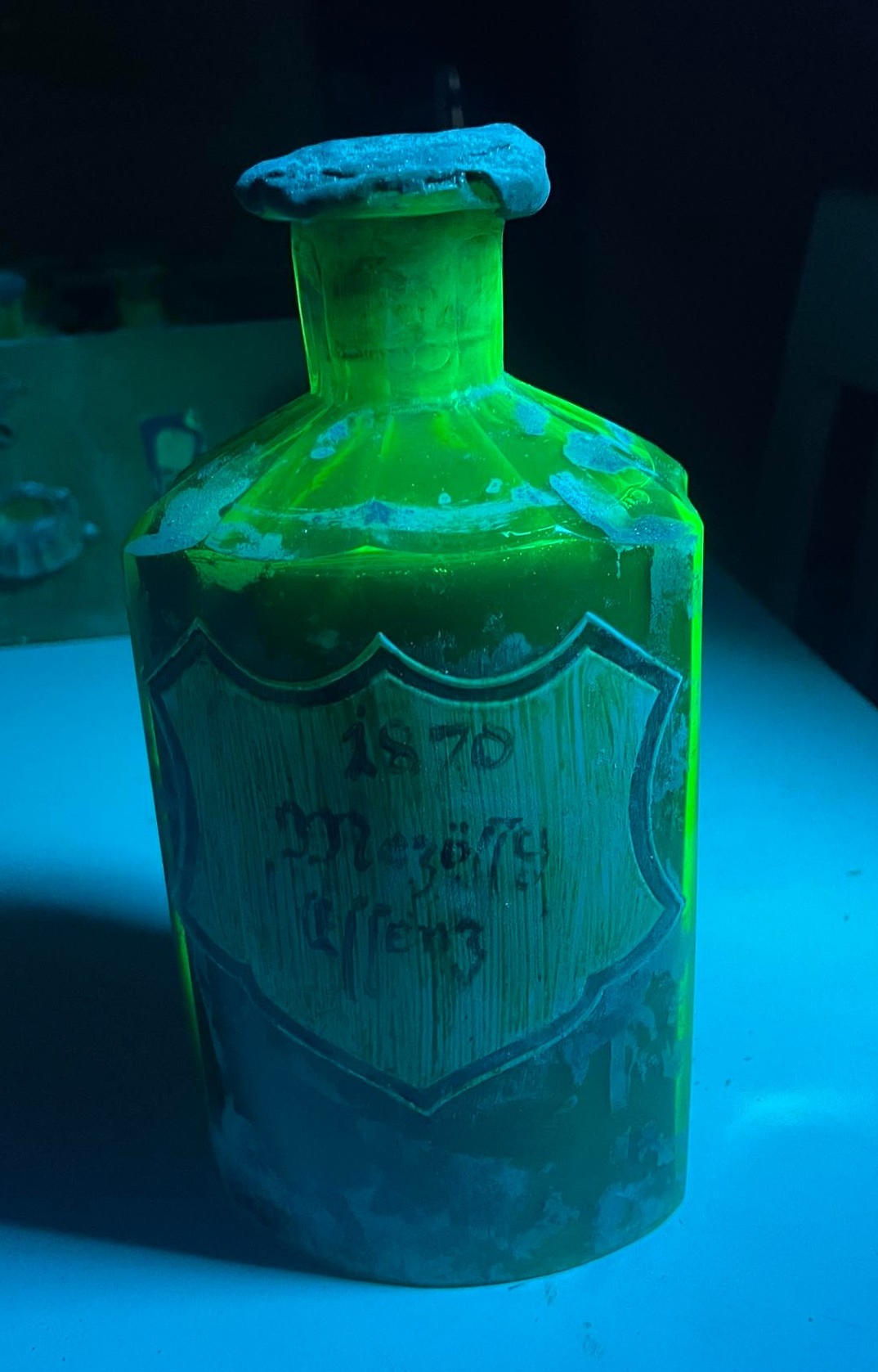 The bottle under UV light, the uranium glass fluorescing green