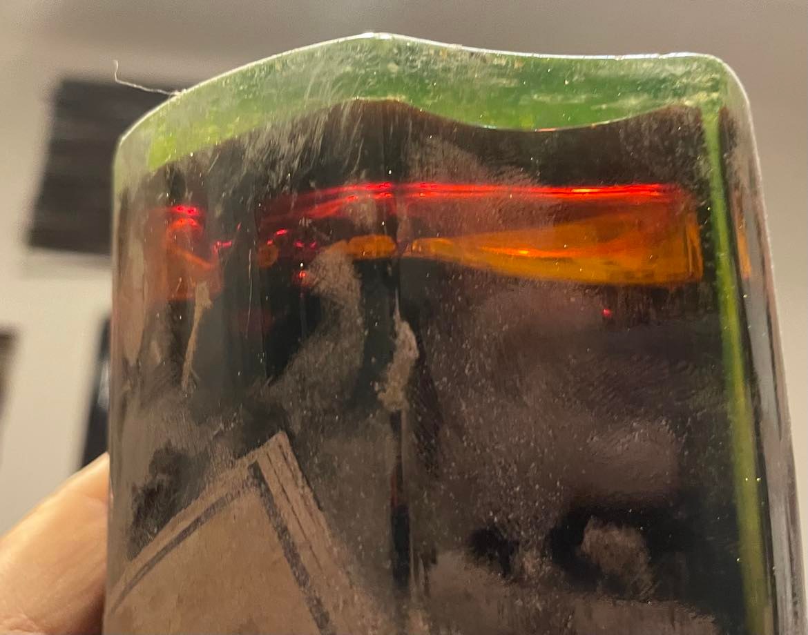 The shoulder of the bottle held to the light, showing the fill level and the colour of the essence