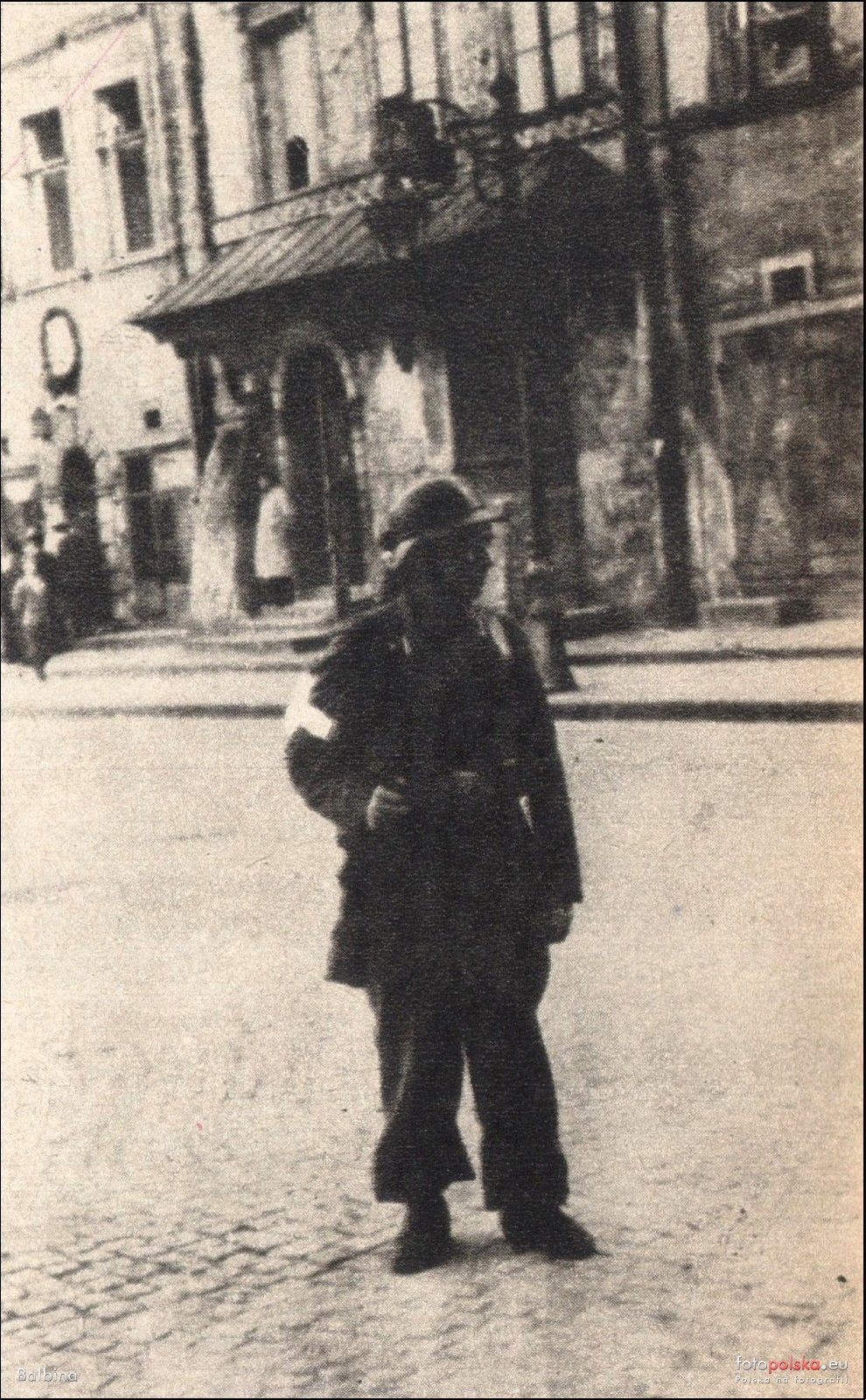 A German sentry with an armband standing on the Old Town Market Square, the Fukier house behind him