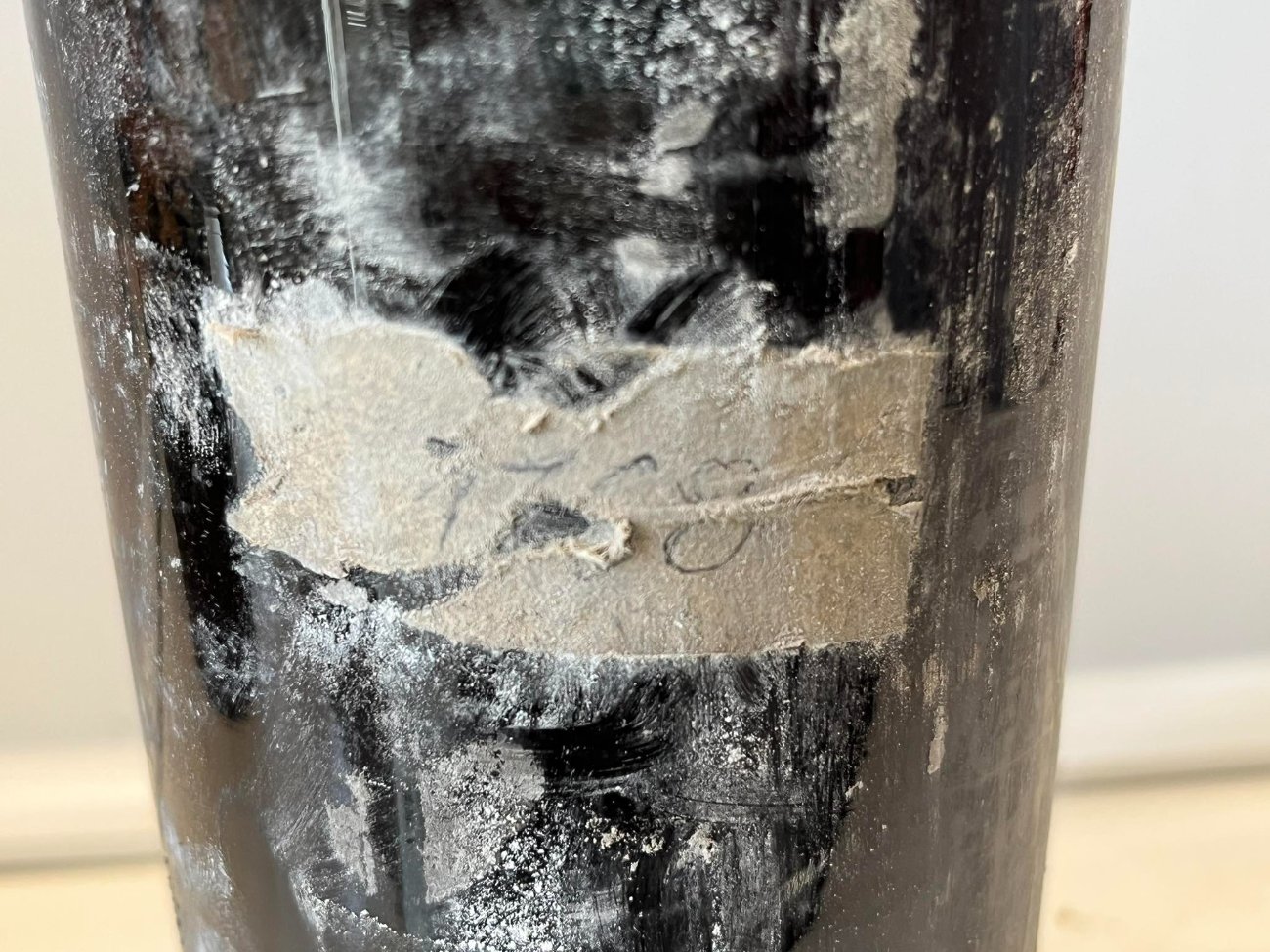 What is left of a paper label on the bottle, rotted to a patch of fibre with pencil strokes