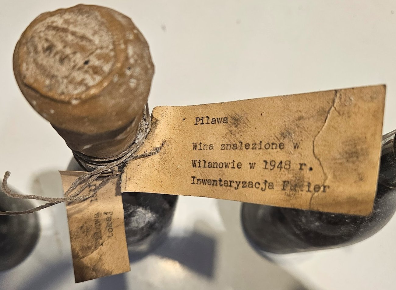 Pilawa tag read clearly: Wina znalezione w Wilanowie w 1948 r. Inwentaryzacja Fukier, tied beside a second tag on the same bottle