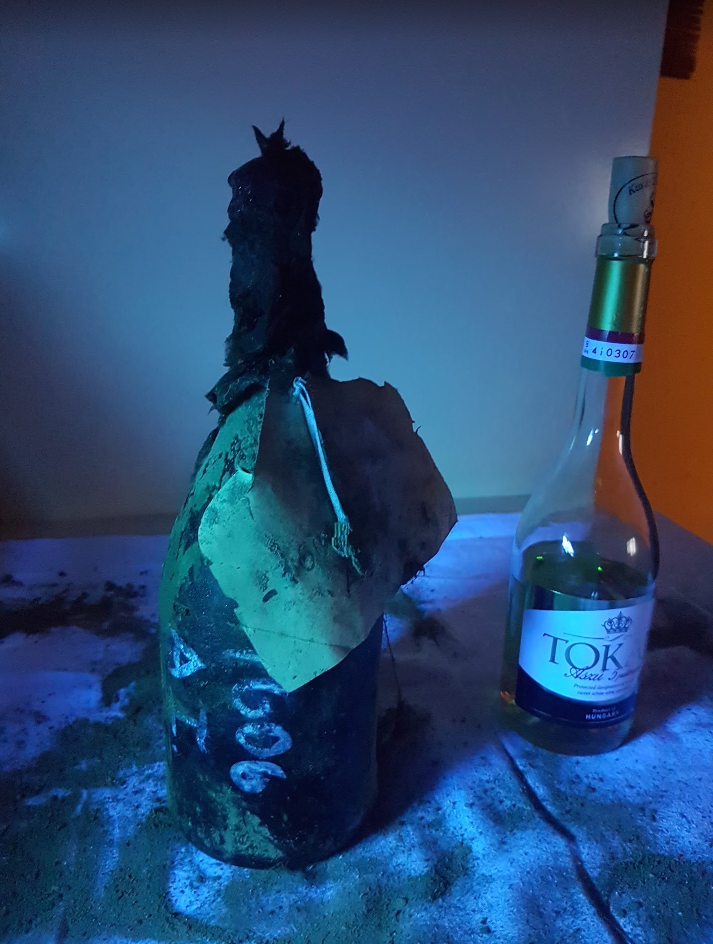 The bottle under ultraviolet light beside a modern Tokaji Aszú bottle