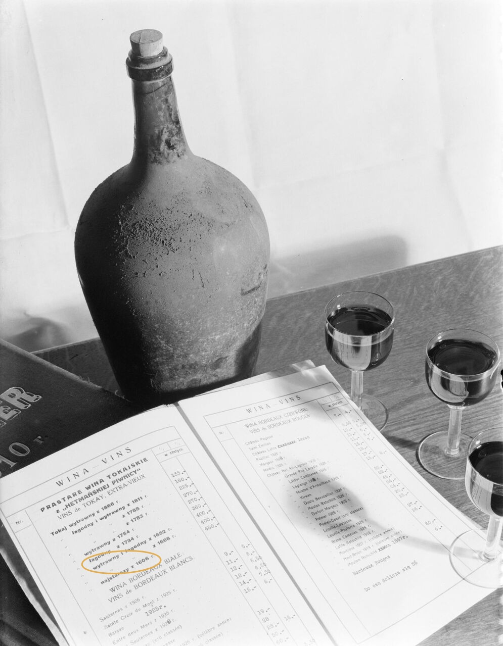 The opened price list photographed beside a mould-covered flagon, the 1606 line marked